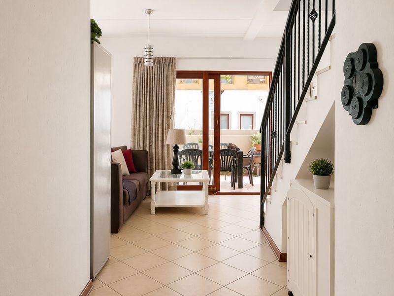 Open-plan living area featuring tiled flooring, a staircase with a metal balustrade, and sliding glass doors leading to an outdoor patio space.