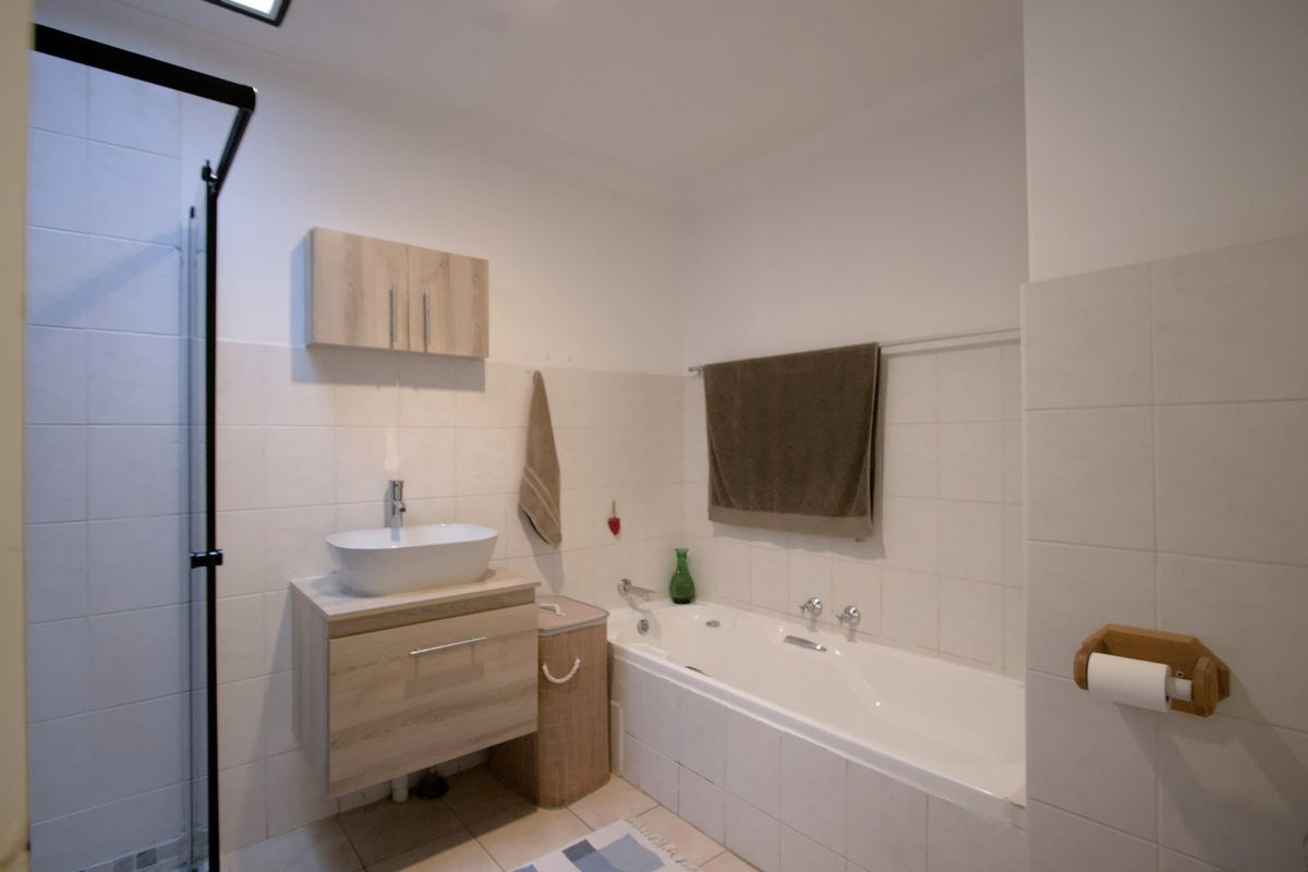 A functional bathroom featuring a built-in bathtub, separate shower enclosure, wall-mounted vanity with vessel sink, and neutral wall tiling.