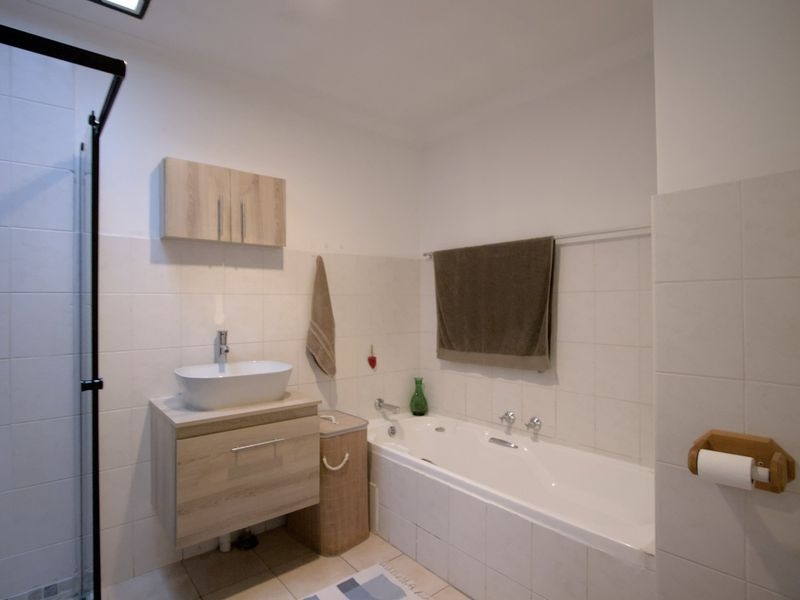 A functional bathroom featuring a built-in bathtub, separate shower enclosure, wall-mounted vanity with vessel sink, and neutral wall tiling.