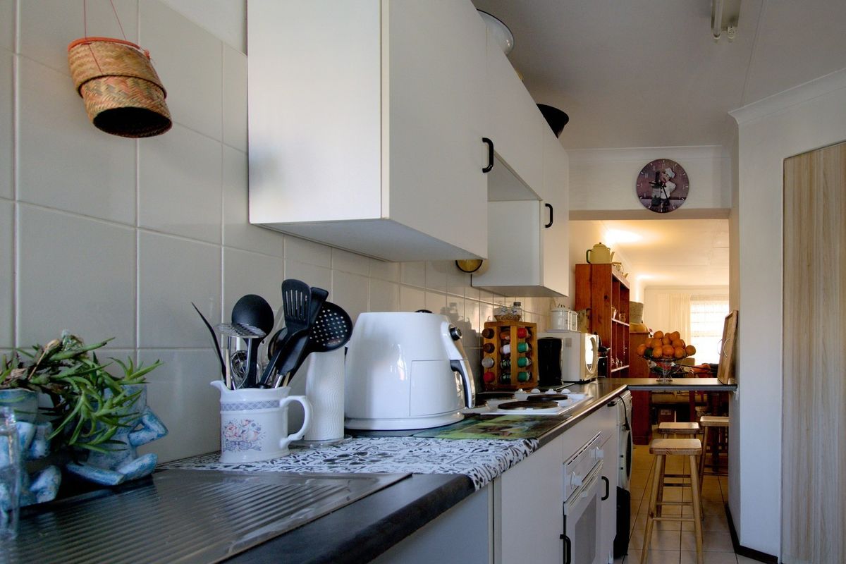 A functional kitchen featuring white cabinetry, tiled backsplash, and built-in cooking appliances, leading into an adjacent living area.