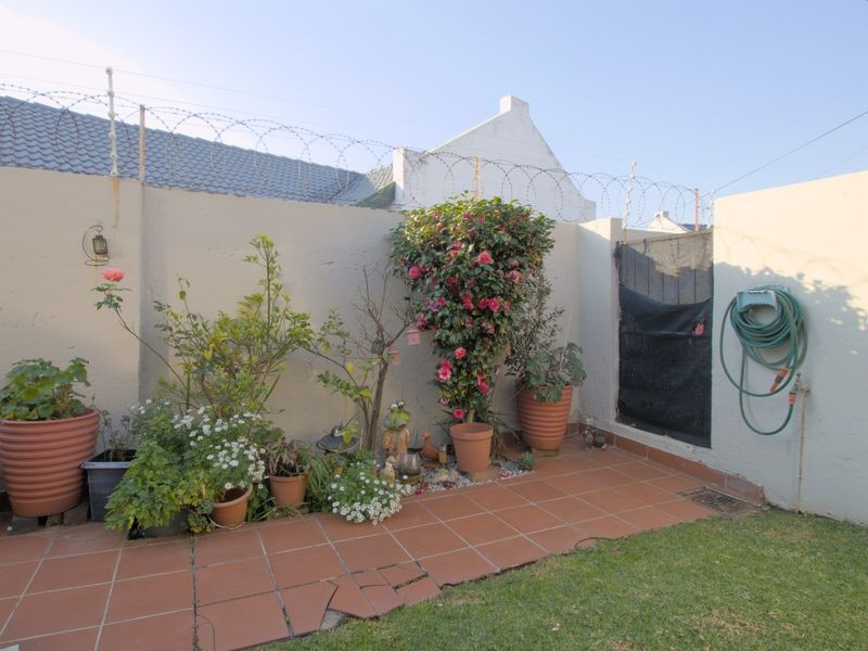 A private rear courtyard featuring a tiled patio area, perimeter wall with security razor wire, and a small garden section.