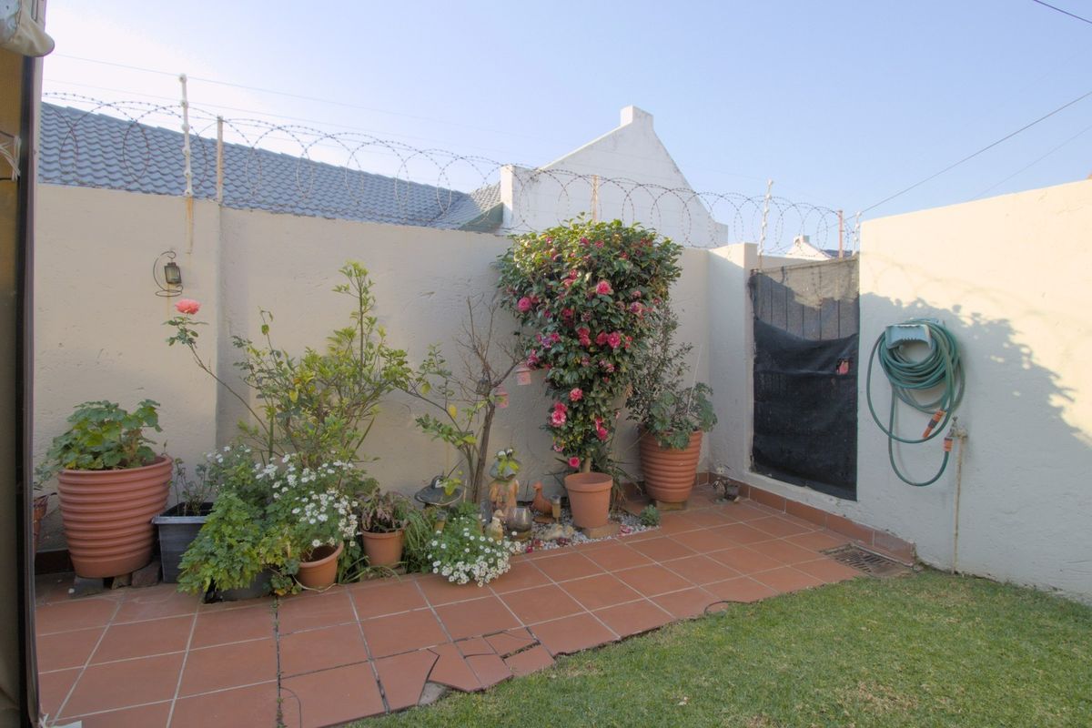 A private rear courtyard featuring a tiled patio area, perimeter wall with security razor wire, and a small garden section.