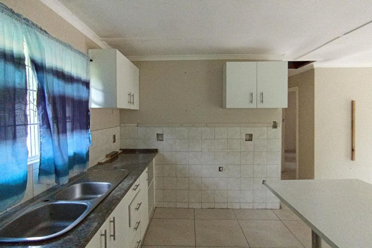 A dated kitchen featuring white cabinetry, a double sink, tiled backsplash, and tiled flooring, currently in need of renovation and finishing touches.