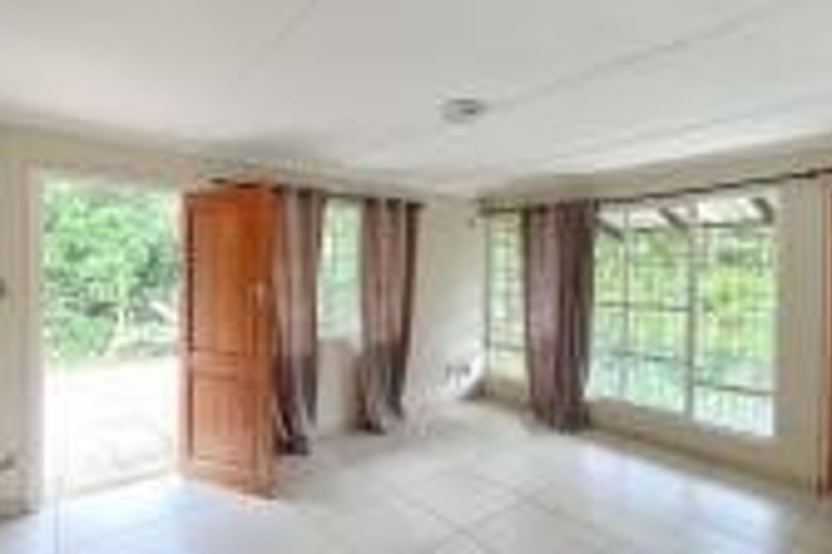A bright, empty living area featuring tiled flooring, timber doors, and large windows providing natural light and garden views.