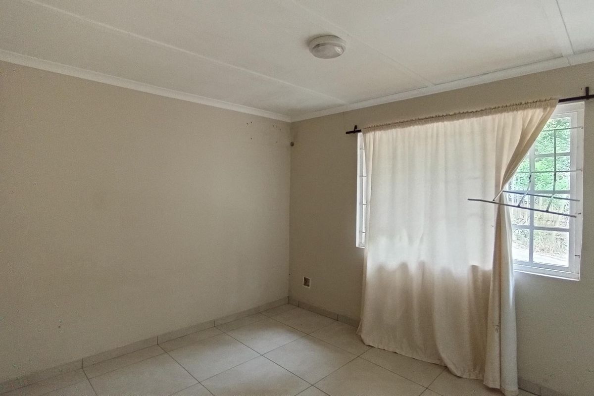 A vacant bedroom featuring neutral tiled flooring, a window with security bars, and a simple ceiling light fixture.