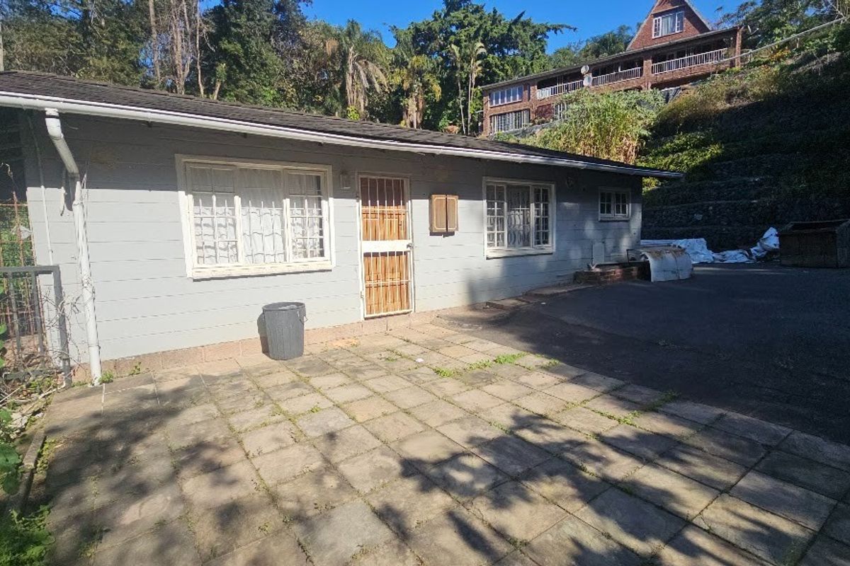Rear exterior view of the property featuring a paved patio area, security gate, and asphalt driveway access.