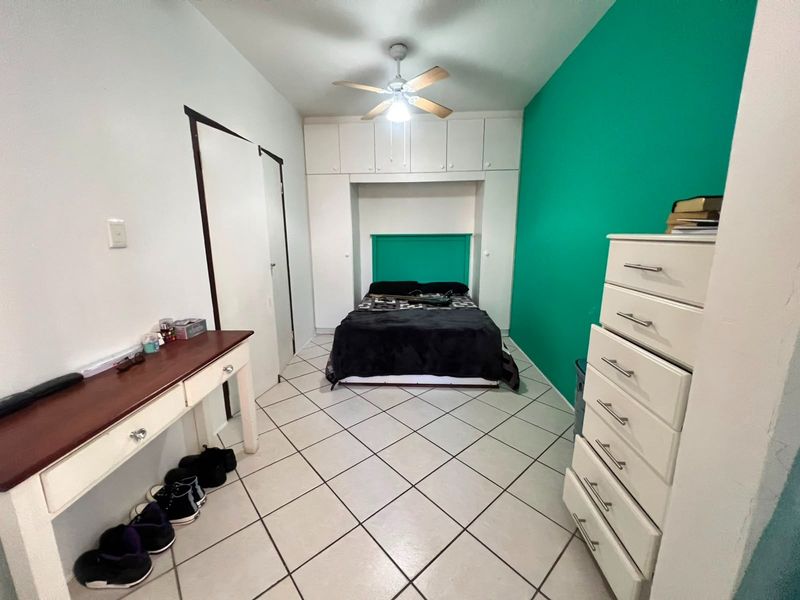 A bedroom featuring built-in cupboards, a ceiling fan, and tiled flooring, with a vibrant green accent wall.