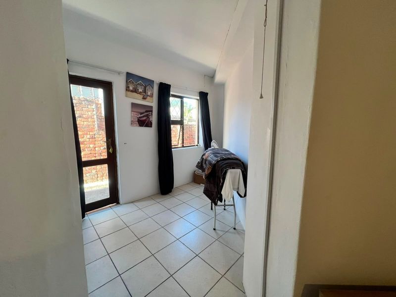 A functional laundry area featuring tiled flooring, a secure exterior door, and a window with burglar bars, providing a practical utility space.
