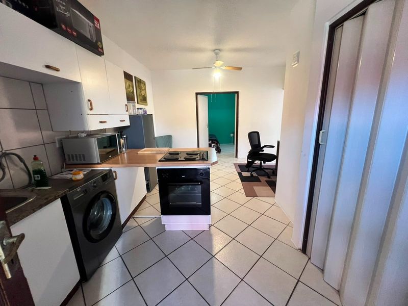 A functional kitchen featuring built-in cabinetry, a hob, an oven, and tiled flooring, leading into an adjacent living area.