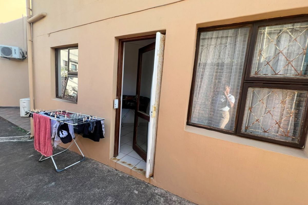 Rear exterior view of the apartment featuring aluminium window frames with security bars and an external access door.