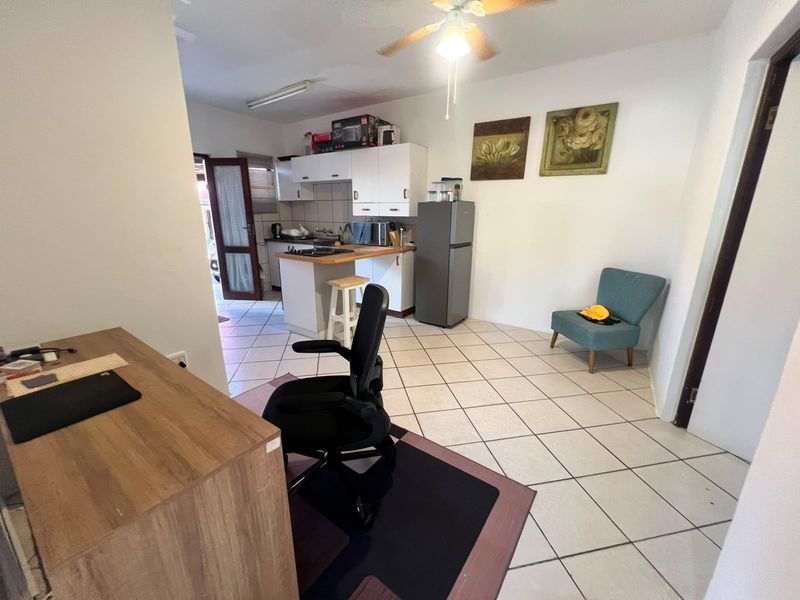 Open plan living area featuring tiled flooring, a ceiling fan, and a compact kitchen with built-in cabinetry and a hob.