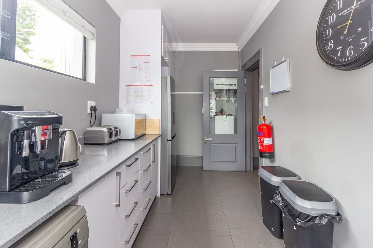 A clean and functional office kitchenette featuring modern grey cabinetry, stone countertops, tiled flooring, and a glass-panelled door leading to a utility area.