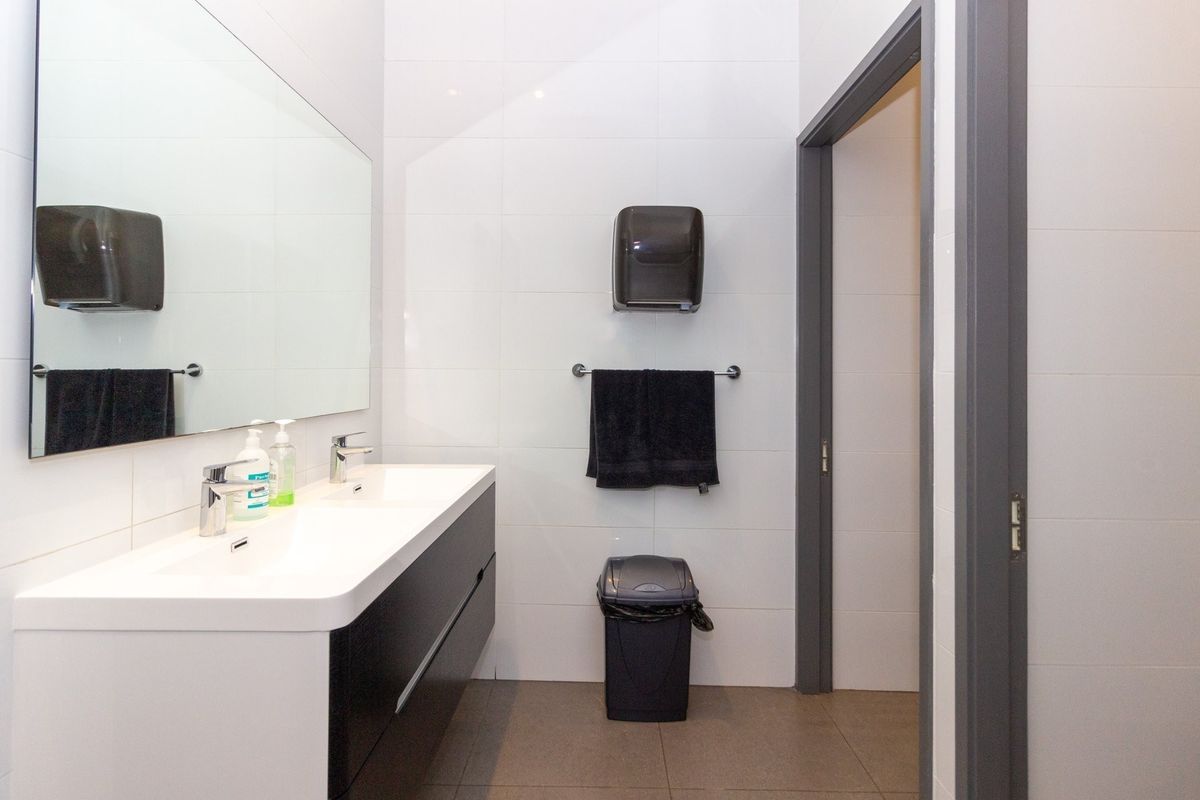 A modern, clean office bathroom featuring a double vanity with integrated sinks, large wall-mounted mirror, and neutral tiled finishes.