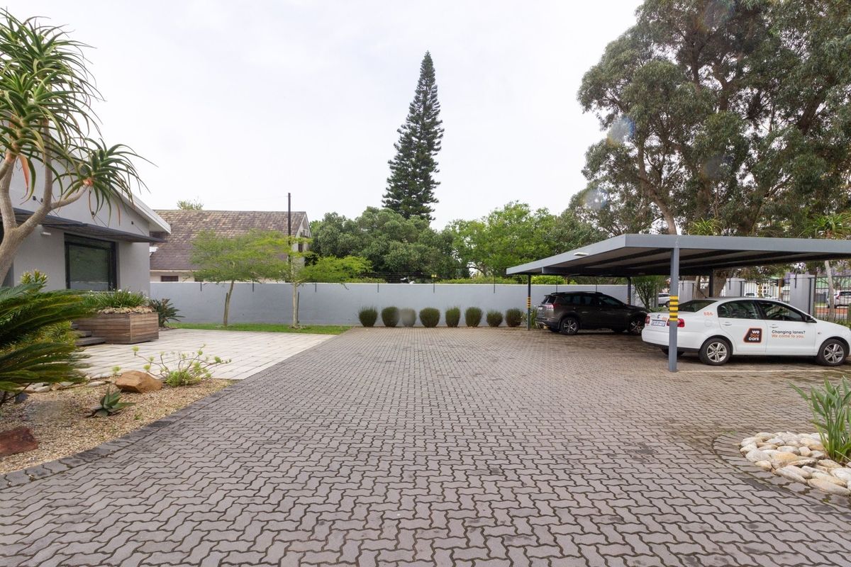 Rear exterior area featuring a paved driveway, a covered carport structure, and a perimeter boundary wall with established garden landscaping.