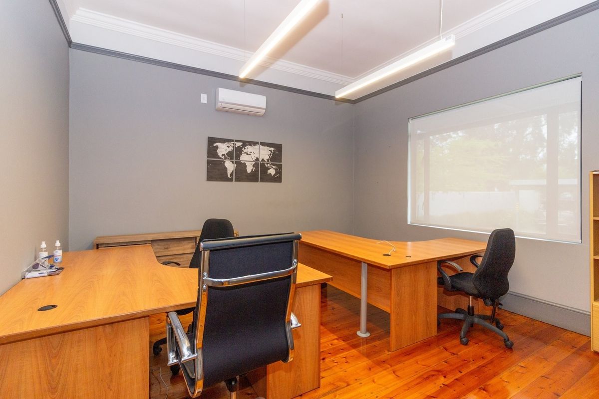 A well-maintained office space featuring polished hardwood floors, crown molding, modern suspended lighting, and a wall-mounted split-system air conditioner.