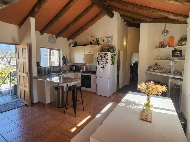 Open-plan kitchen and living area featuring exposed timber ceiling beams, tiled flooring, granite countertops, and built-in cabinetry with direct access to an outdoor balcony.