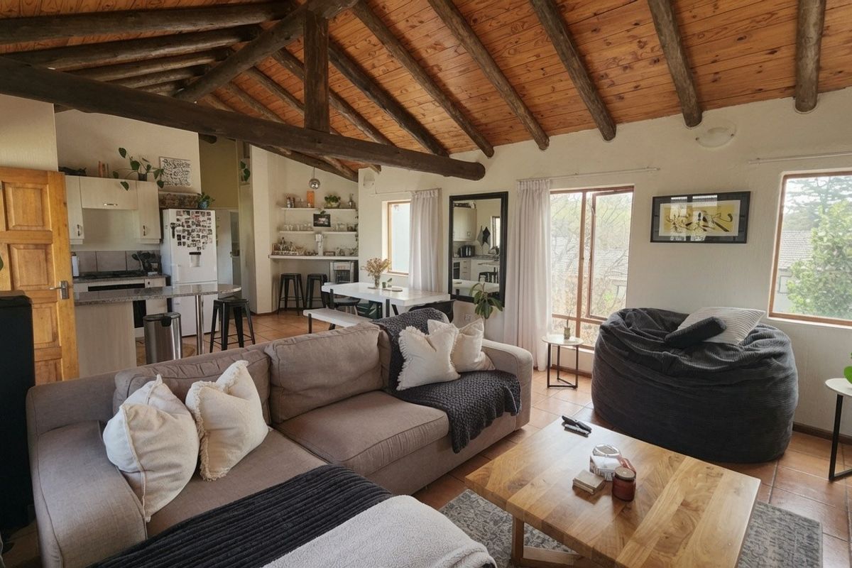 Open-plan living and kitchen area featuring high exposed timber beam ceilings, tiled floors, and natural light through large windows.