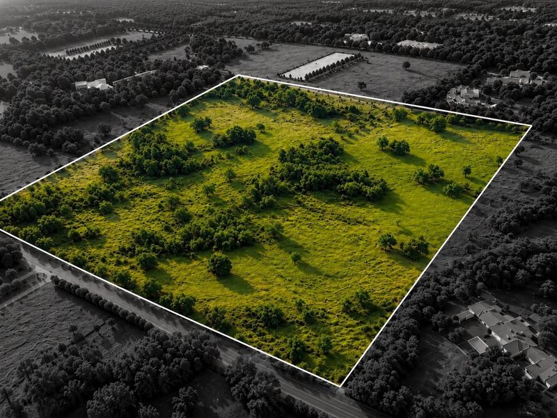 An aerial view of a large, undeveloped residential land plot featuring natural vegetation and mature trees, highlighted against the surrounding landscape.