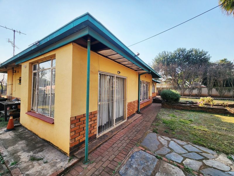 Rear exterior view of the house featuring a brick and plaster facade, paved walkway, and established garden area with stone retaining walls.