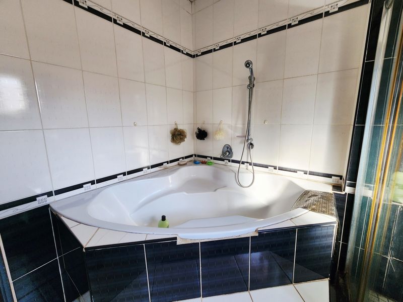 A corner bathtub featuring a handheld shower fixture, finished with black and white ceramic tiling.