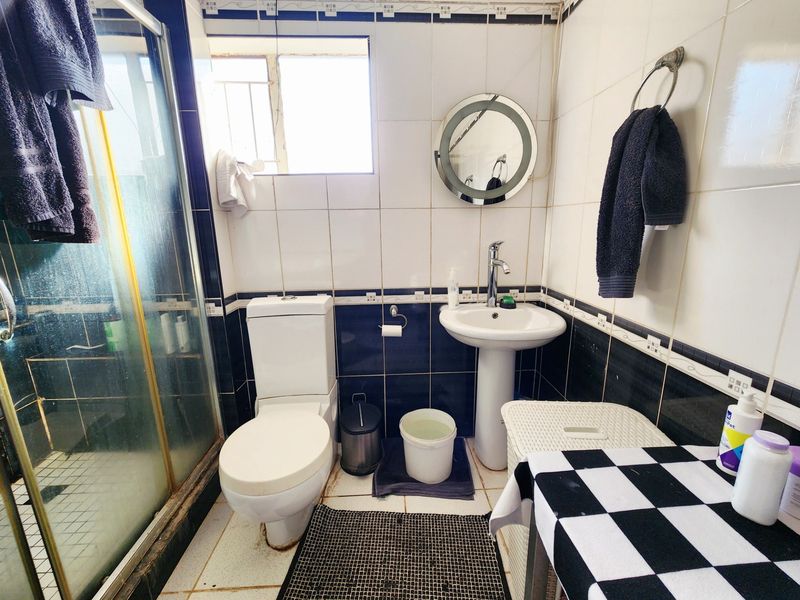A compact bathroom featuring a pedestal basin, toilet, and a glass-enclosed shower with contrasting blue and white wall tiling.