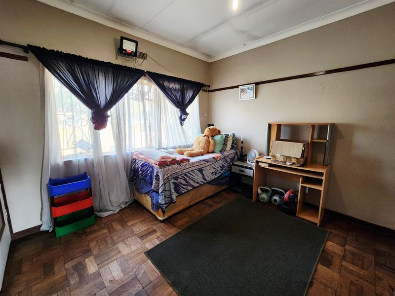 A bedroom featuring classic parquet flooring, a picture rail, and security bars on the window, offering a functional space with potential for cosmetic updates.