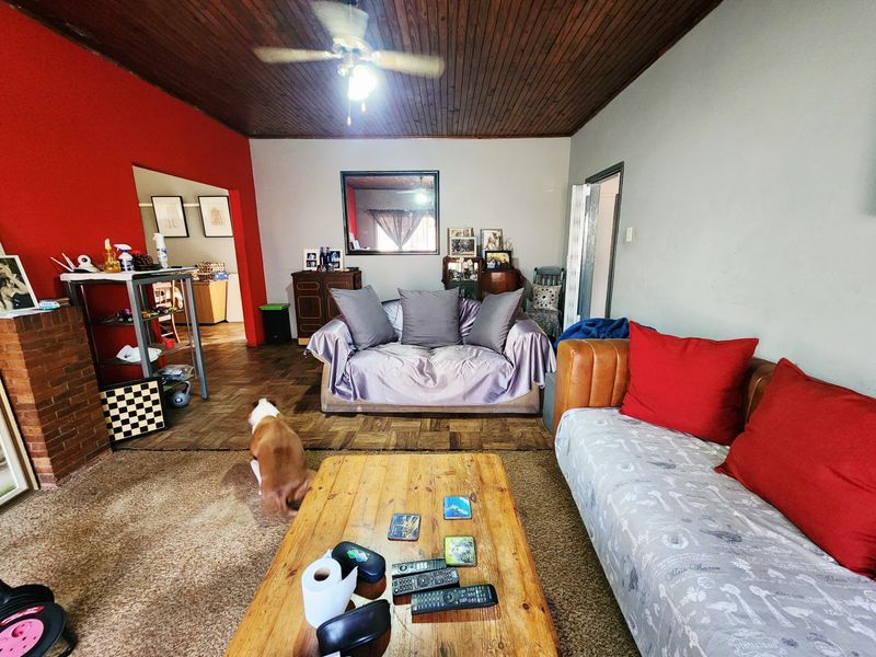 Living room featuring a timber ceiling, ceiling fan, parquet flooring, and a brick fireplace, offering a dated but functional space.