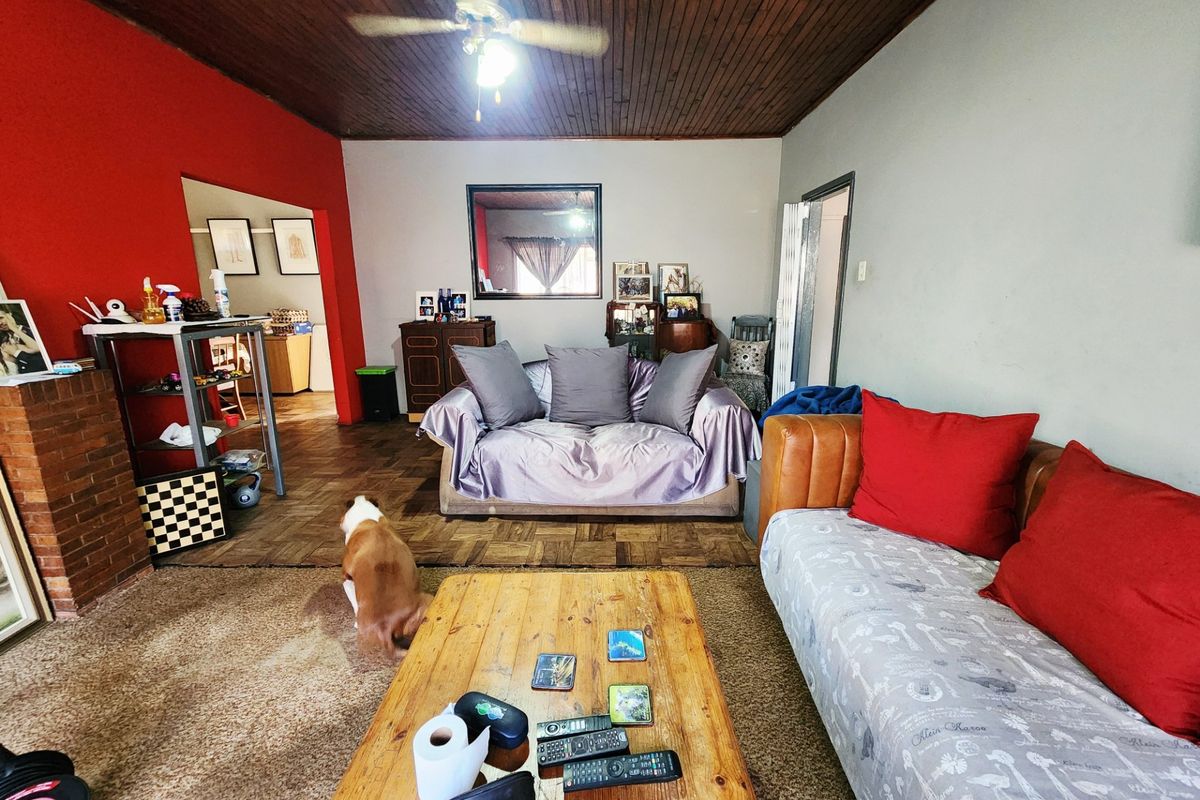 Living room featuring a timber ceiling, ceiling fan, parquet flooring, and a brick fireplace, offering a dated but functional space.