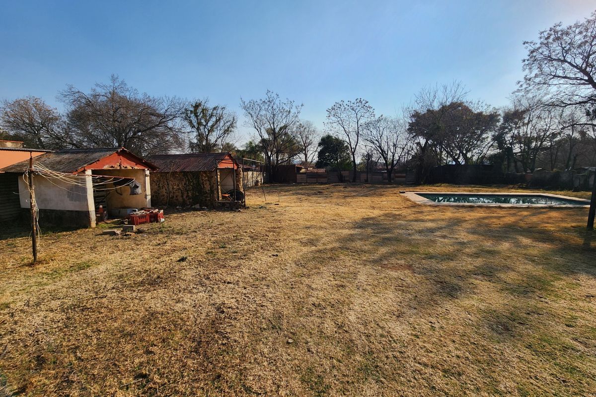 Spacious rear garden featuring a swimming pool and a detached outbuilding requiring maintenance and repair.
