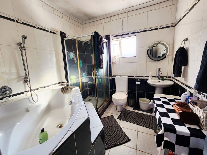 A dated bathroom featuring a corner bathtub, separate glass shower enclosure, pedestal basin, and toilet with tiled finishes throughout.