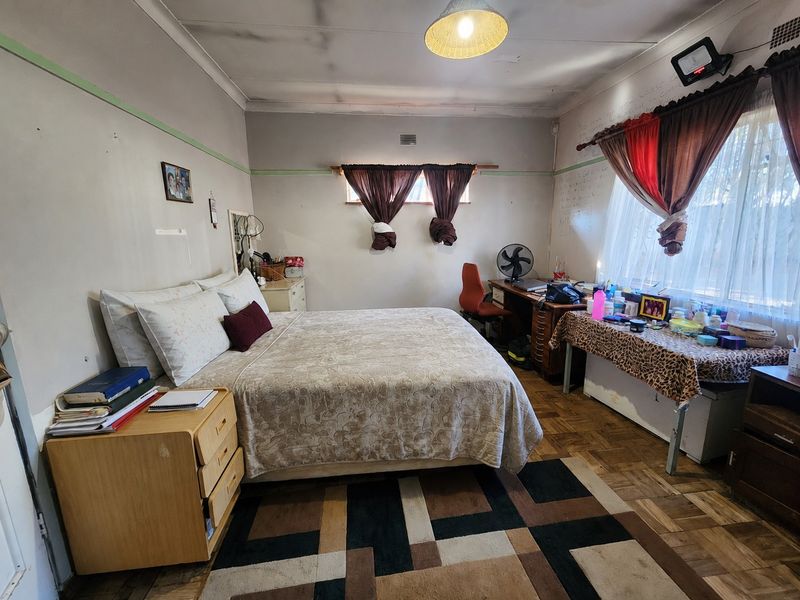 A bedroom featuring parquet flooring and ceiling cornice, currently showing signs of wear including ceiling water staining and wall surface damage.