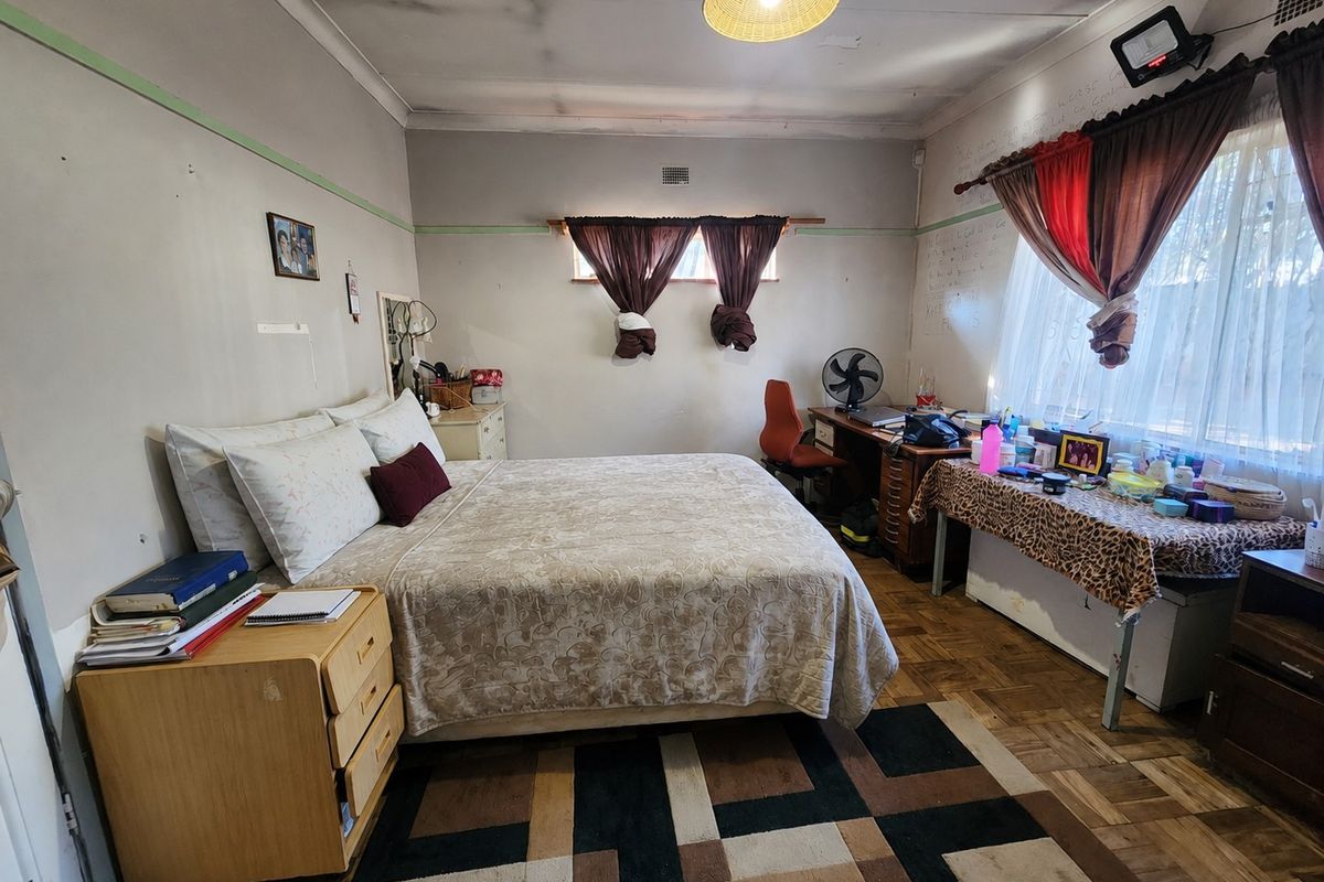 A bedroom featuring parquet flooring and ceiling cornice, currently showing signs of wear including ceiling water staining and wall surface damage.
