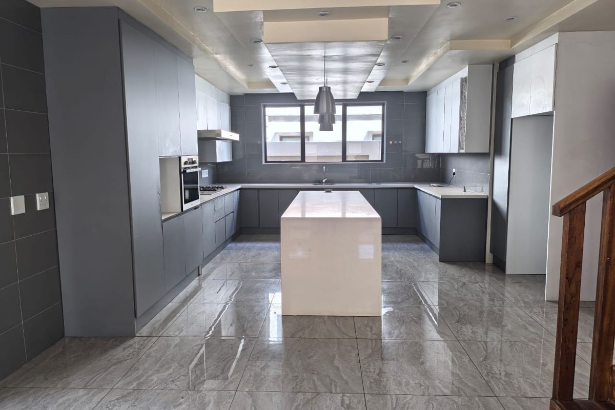 Modern, spacious kitchen featuring a central island, sleek grey cabinetry, built-in oven, and polished tile flooring with a contemporary drop ceiling design.