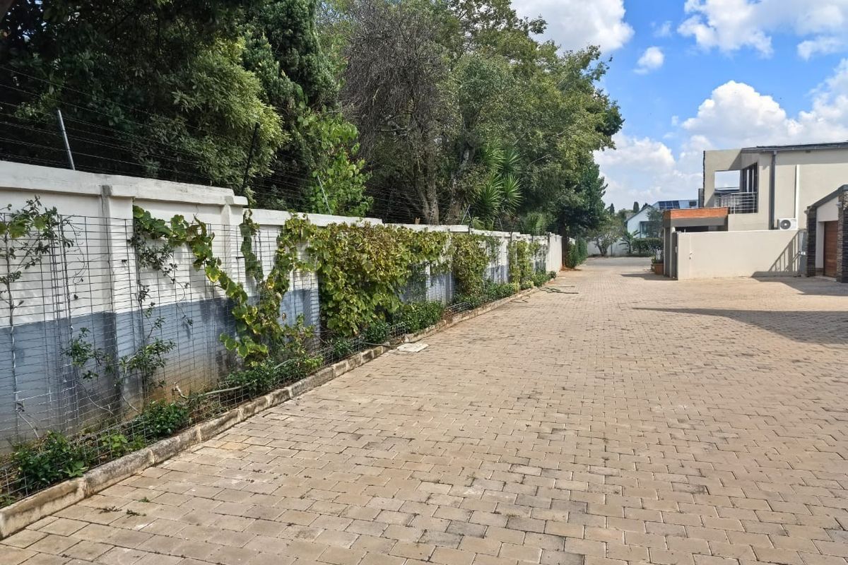 A paved driveway area featuring a long perimeter wall with integrated electric fencing and a trellis system for climbing plants.
