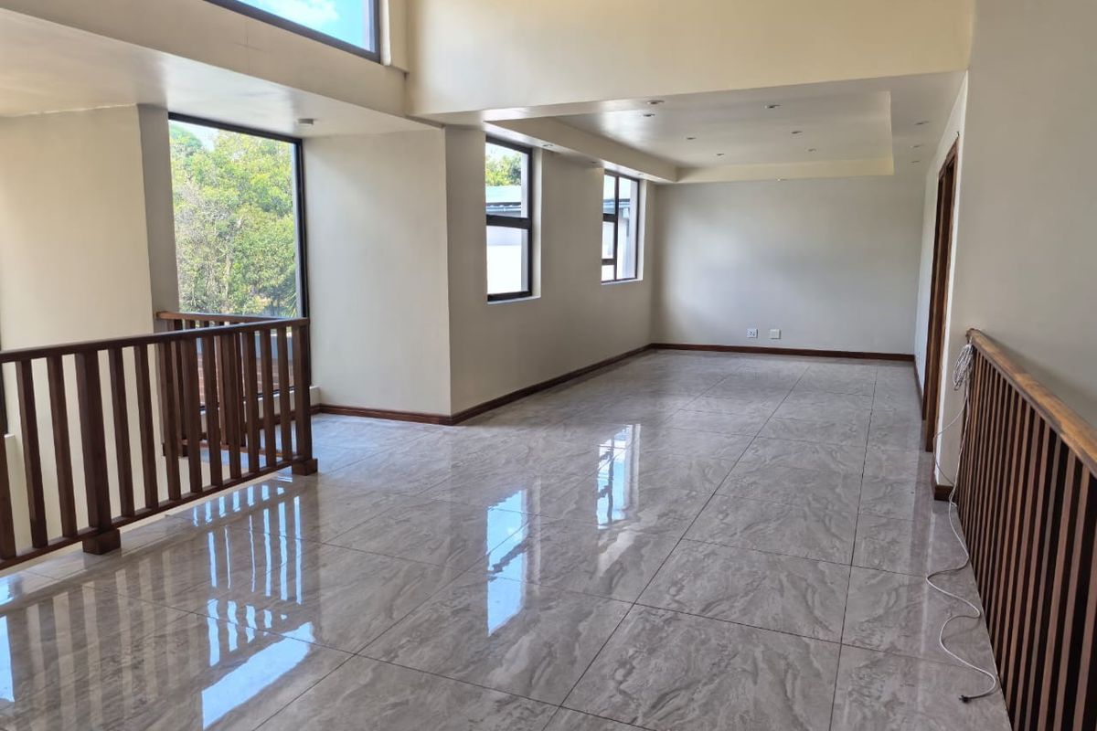 Spacious, light-filled living area featuring polished tiled flooring, high ceilings, and a wooden balustrade overlooking the lower level.