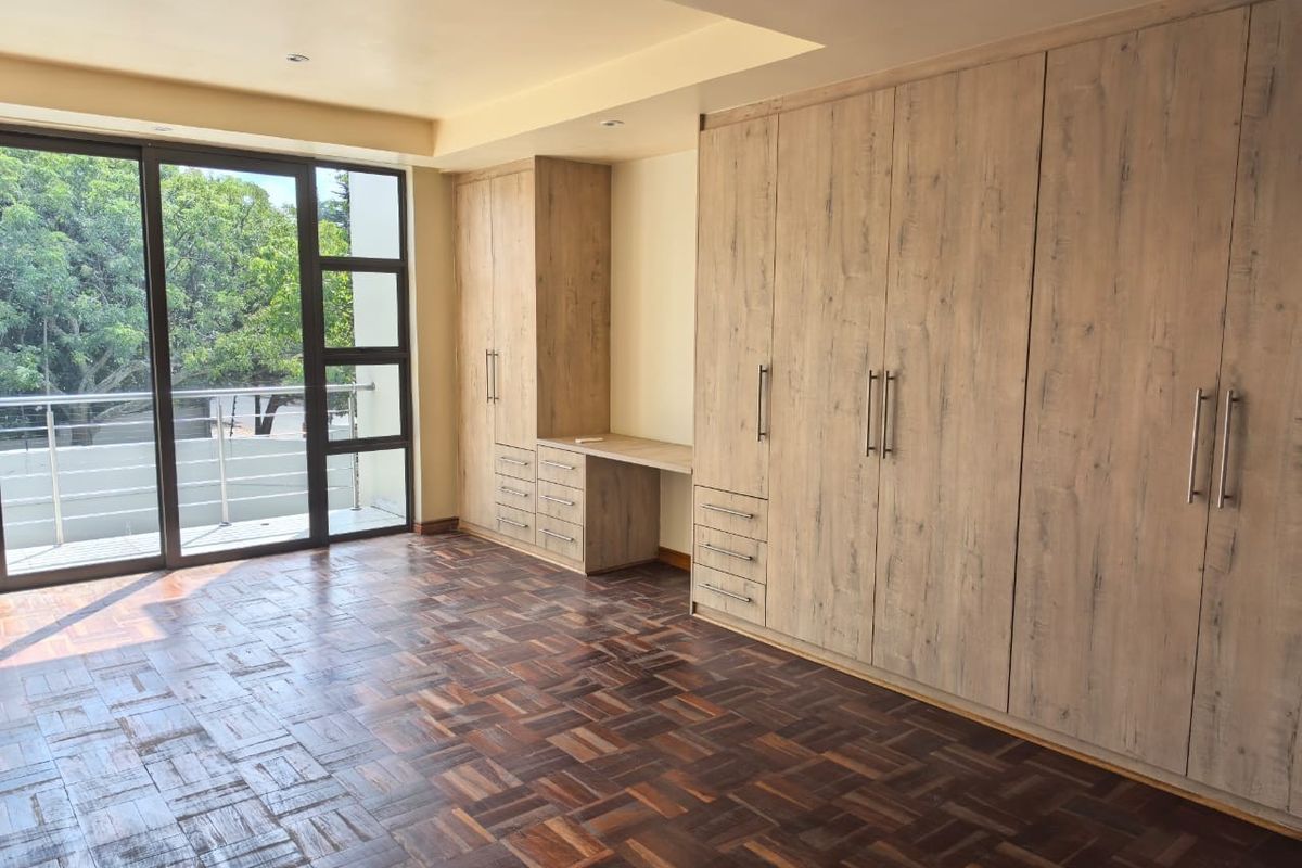 Spacious bedroom featuring warm parquet flooring, extensive built-in cabinetry with an integrated desk, and large sliding doors opening to a private balcony.