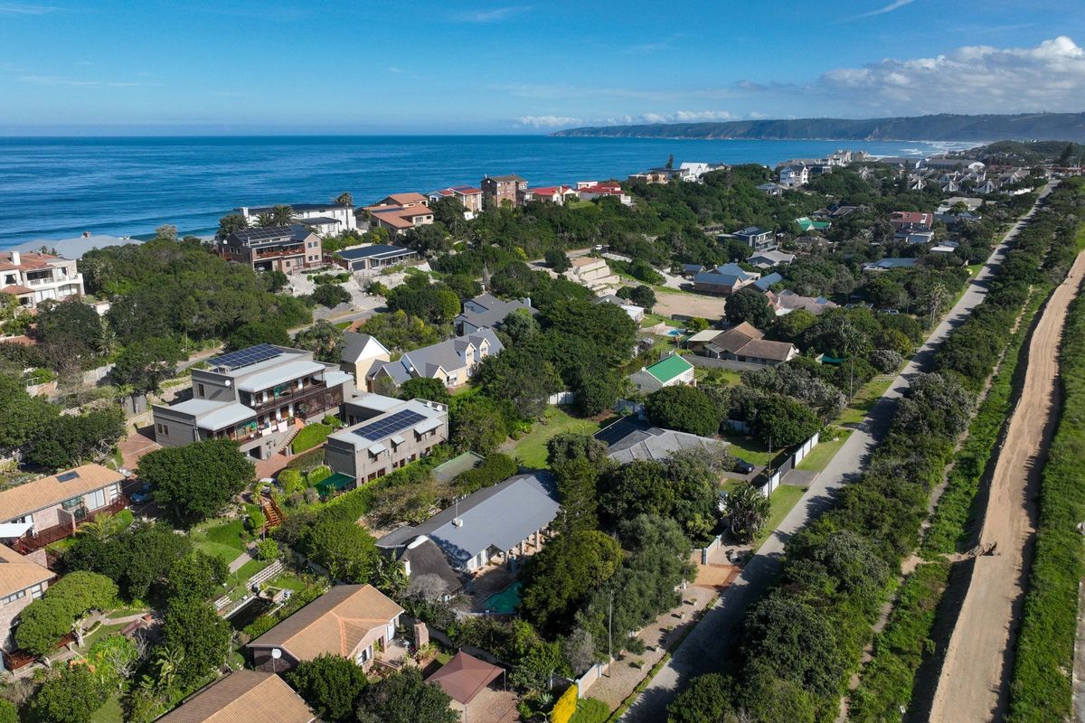 An aerial view of a coastal residential neighborhood featuring homes with solar panels, surrounded by lush greenery and proximity to the ocean.