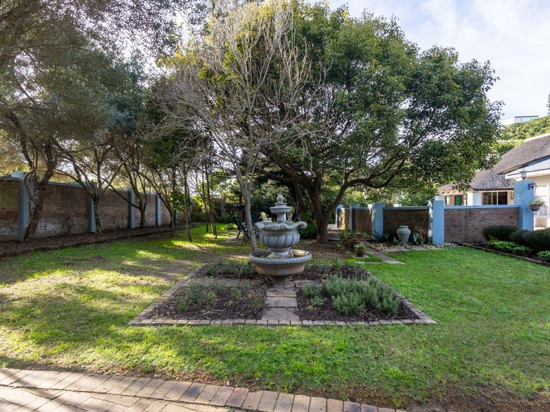 A spacious garden featuring a central stone fountain, mature trees, and brick boundary walls, offering a private and established outdoor setting.