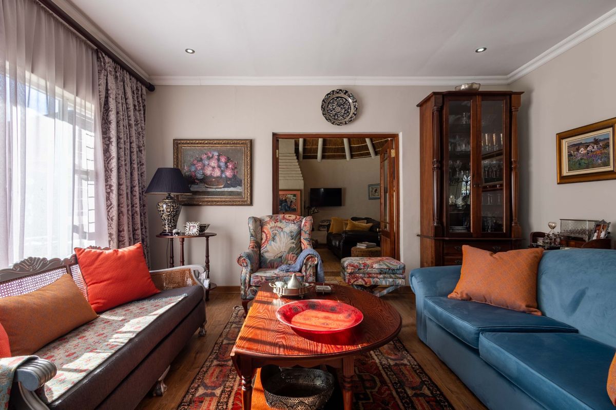 A cozy living room featuring timber flooring, recessed downlighting, and decorative cornice, with an open doorway leading to an adjacent living space.