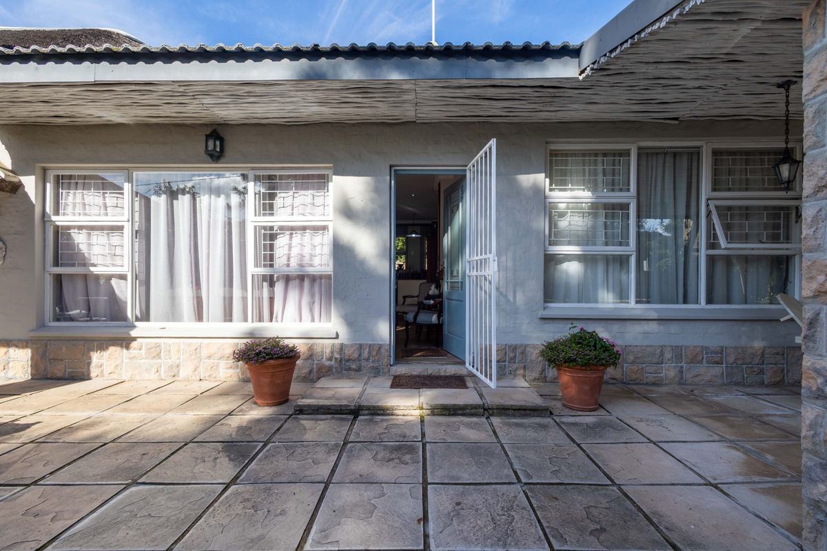 A rear exterior view featuring a paved patio area, stone-clad base, and a secure entrance door with a security gate.