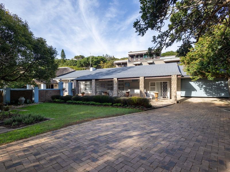 Front view of a single-story residence featuring a paved driveway, covered patio with stone pillars, and a well-maintained garden.