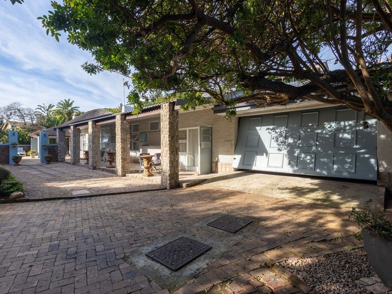 Front exterior view featuring a paved driveway, covered patio area with stone pillars, and a garage entrance.