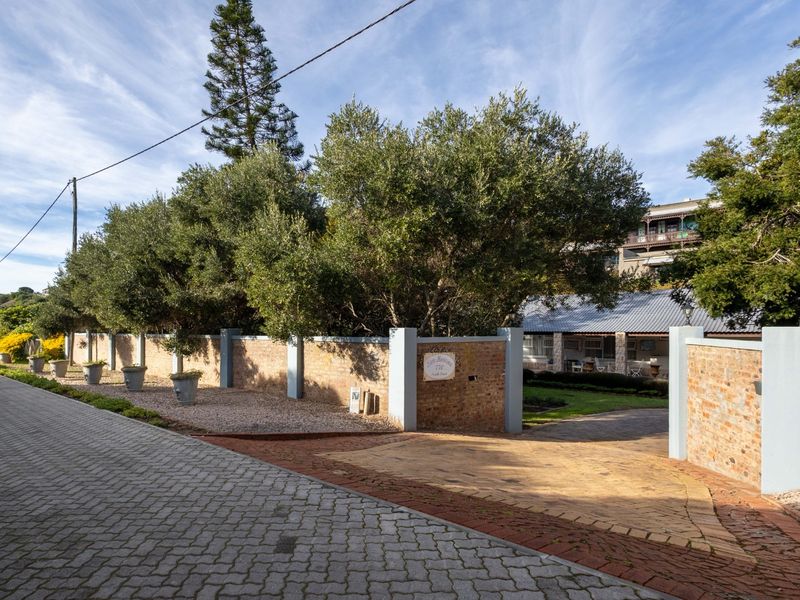 Street view of the property entrance featuring a brick boundary wall, paved driveway, and established trees.