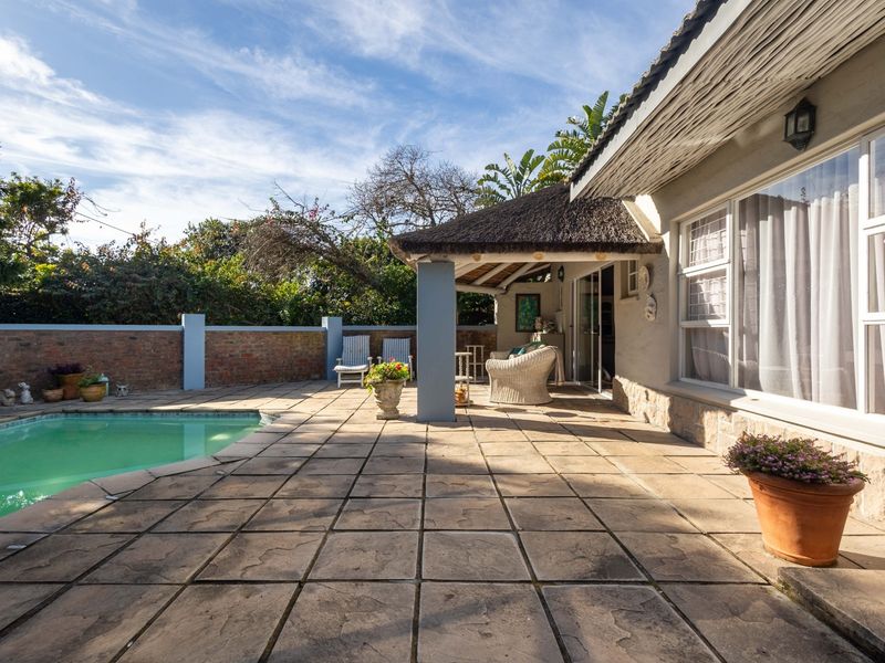 Outdoor entertainment area featuring a swimming pool, paved patio, and a covered thatched roof veranda, ideal for relaxation and hosting.