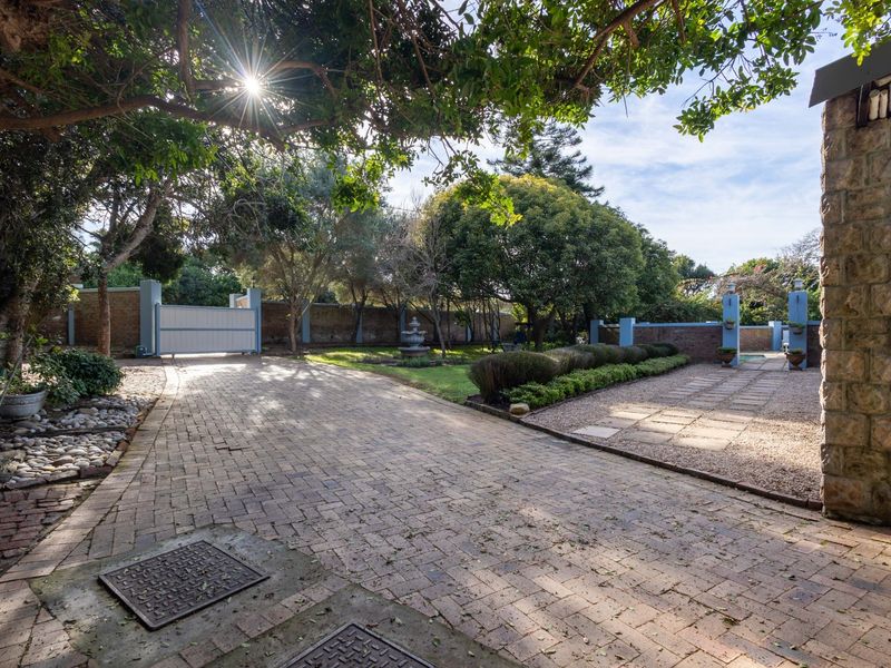 Spacious front driveway featuring paved surfaces, stone-clad exterior wall, and established garden surroundings with secure gated access.