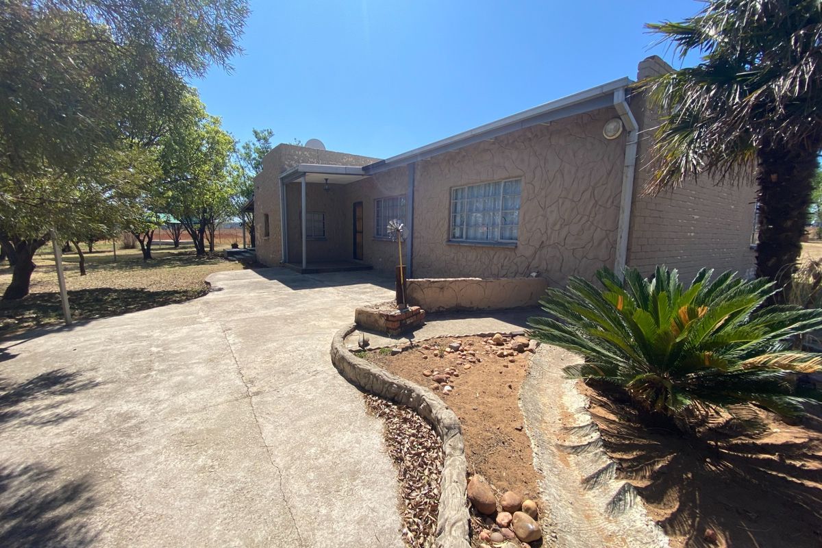 Rear view of the property featuring a textured facade, covered patio area, and a concrete driveway leading to the garden space.