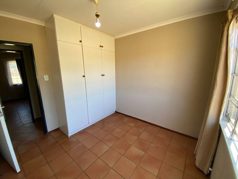 A clean, empty bedroom featuring built-in cupboards, tiled flooring, and neutral wall finishes, offering a versatile space ready for personalization.