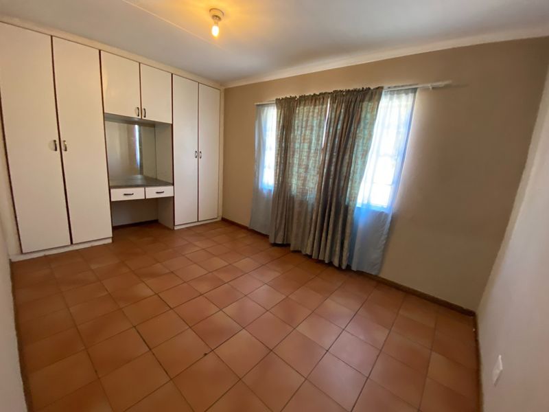 A spacious bedroom featuring built-in cupboards with an integrated vanity unit and durable tiled flooring, offering a clean and functional living space.
