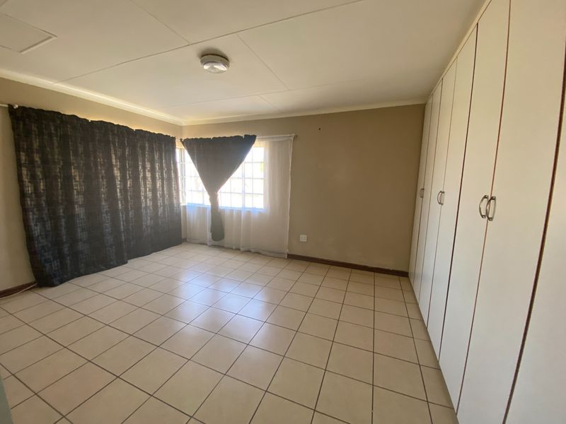 A spacious, empty bedroom featuring neutral tiled flooring and extensive built-in cupboard storage, offering a clean canvas for personalization.