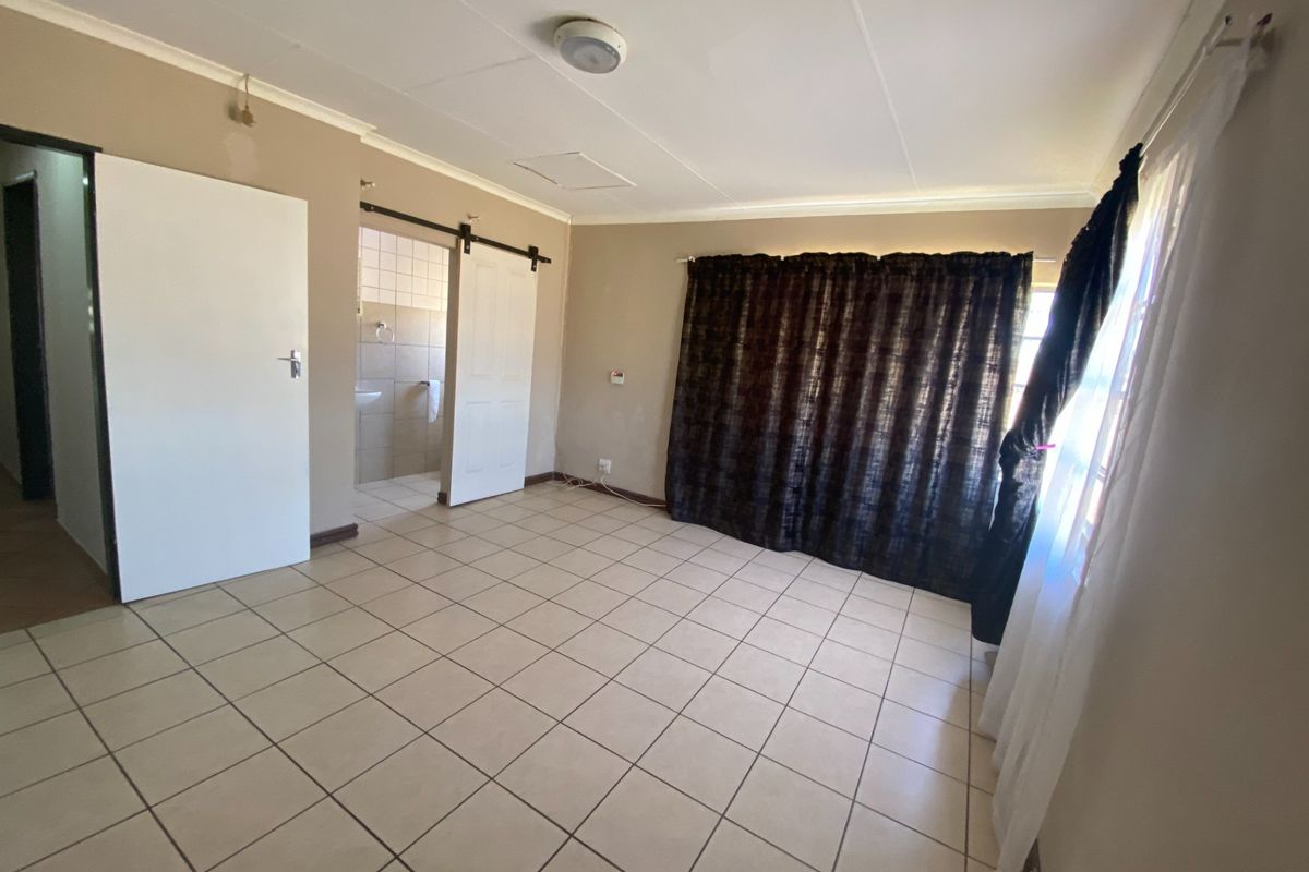 An empty bedroom featuring tiled flooring, a sliding barn door leading to an en-suite bathroom, and neutral wall finishes.